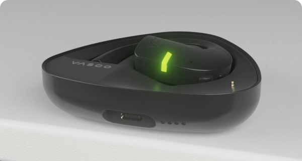 Een Vasco Translator E1-oordopje wordt in de oplaadcase geplaatst. De knipperende LED-lampjes geven het huidige batterijniveau van de case en het oordopje aan. 