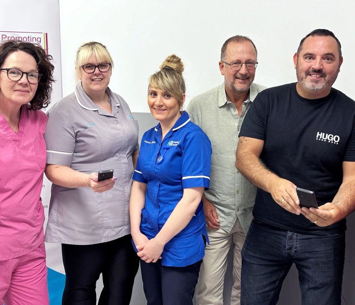 Vijf lachende mensen staan samen in zorgkleding, waarvan twee een vertaalapparaat vasthouden.