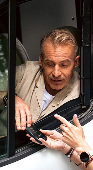 Een man zit in een auto en praat tegen het Vasco Q1-apparaat dat iemand hem aanreikt.