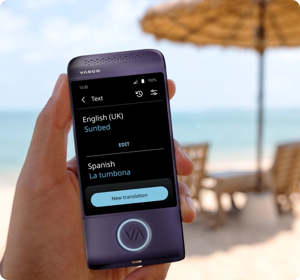 Een close-up van een hand die een paars elektronisch vertaalapparaat van het merk Vasco vasthoudt. Op het scherm is een tekstvertaling te zien van het Engels (VK) naar het Spaans, waarbij het woord 